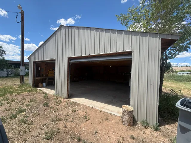 Metal-sided outbuilding featuring two garage door openings, a concrete apron, and an overhanging eave