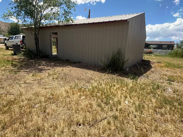 Metal-sided structure with a sloped metal roof, featuring an open doorway and a surrounding land area