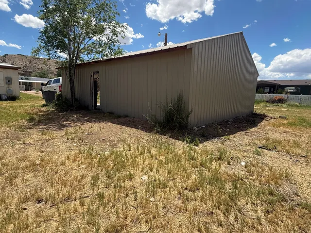 Corrugated metal utility building with a pitched roof, featuring an open doorway and a surrounding natural landscape