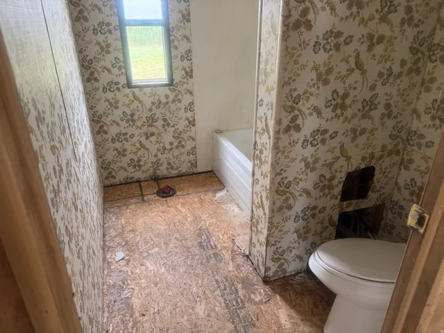 Bathroom space featuring a window, a white bathtub, and patterned wallpaper