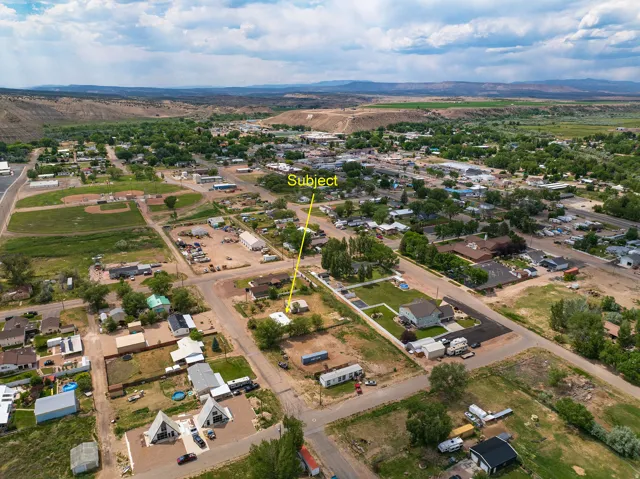 Aerial perspective showcasing the property within the local landscape, featuring residential structures, surrounding green spaces, and distant natural terrain