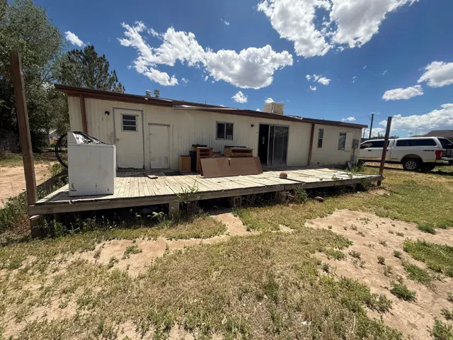 Rear exterior featuring a full-width wood deck, white vertical siding, and a brown trim roofline