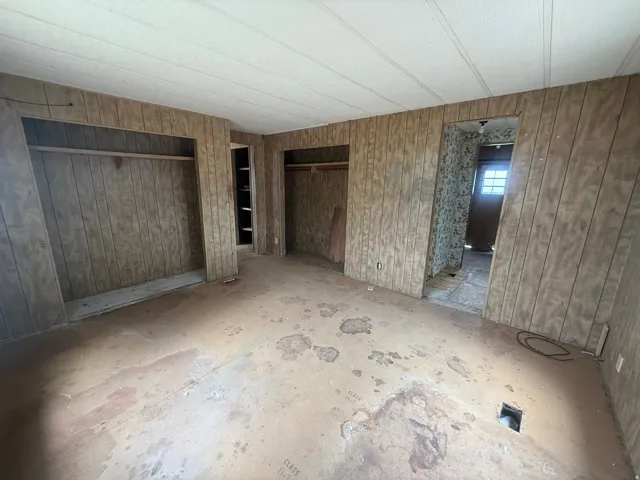 Room featuring vertical wood paneling, open closet spaces with hanging rods, and a ceiling with linear paneling