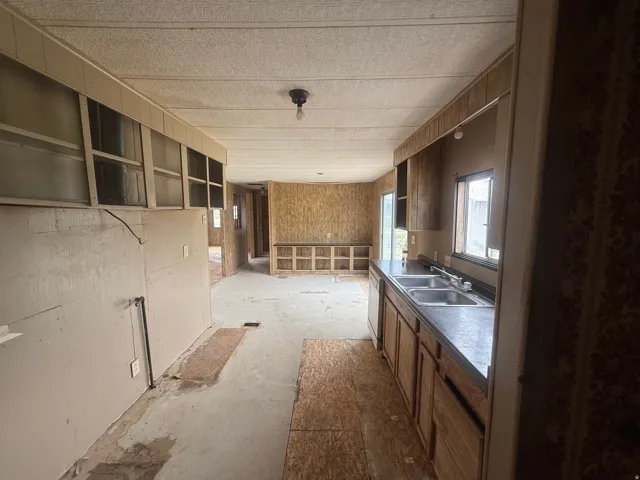 Kitchen area with a double basin sink, dark countertop, and wood-finish cabinetry