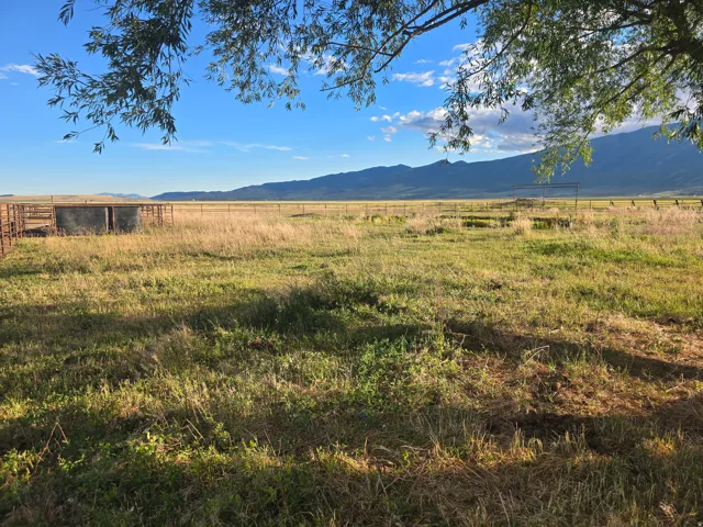 Expansive agricultural land featuring a large fenced enclosure, two prominent water troughs, and surrounding mountain ranges