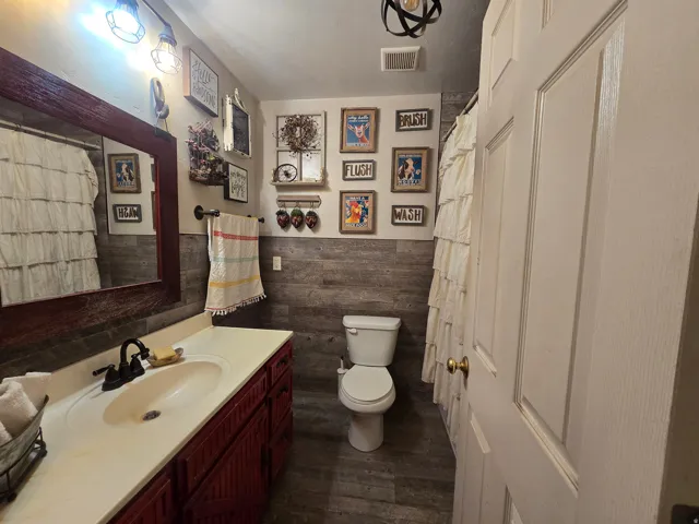 Bathroom featuring wood-finish accent wall, white countertop vanity with dark red cabinetry, wood-framed mirror, and wood-finish flooring