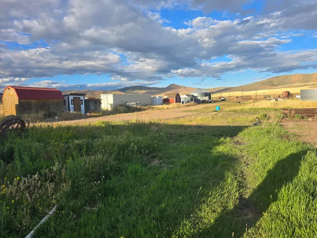 Expansive land featuring a grassy foreground, multiple outbuildings, and a mountainous backdrop