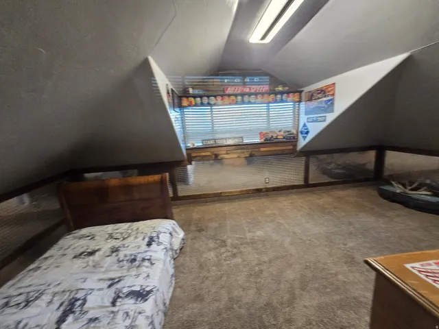 Attic space featuring sloped ceilings, recessed window with horizontal blinds, wood-finish trim, and corrugated metal wall paneling