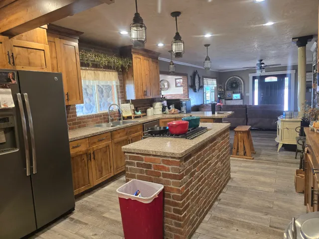 Open-concept kitchen and living area featuring a brick island with integrated cooktop, wood-finish flooring, and recessed lighting