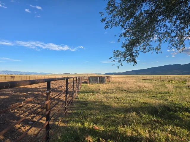 Expansive property featuring a rustic metal fence, grazing land, and a mountain backdrop