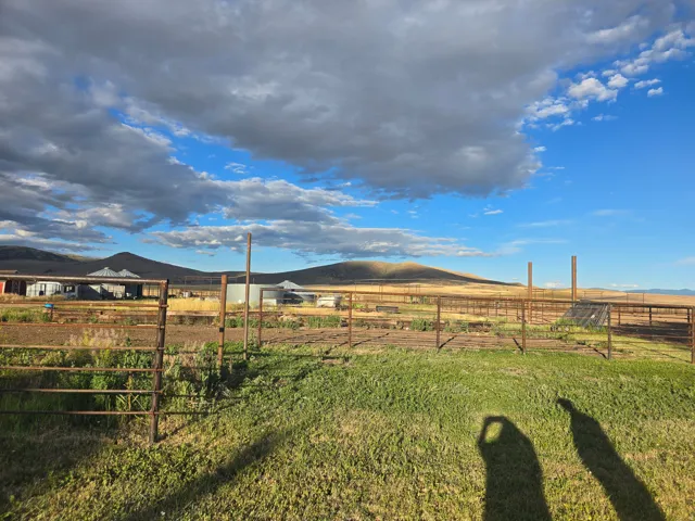 Expansive property featuring verdant foreground, fencing, and distant structures, all set against a backdrop of rolling hills and open sky