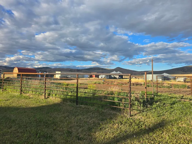 Expansive fenced property with multiple agricultural buildings, mature landscaping, and mountainous surroundings