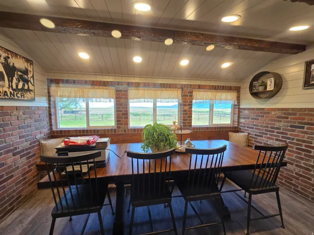 Dining area featuring exposed brick walls, wood-finish flooring, a built-in wooden bench, a sloped ceiling with recessed lighting, and exposed ceiling beams
