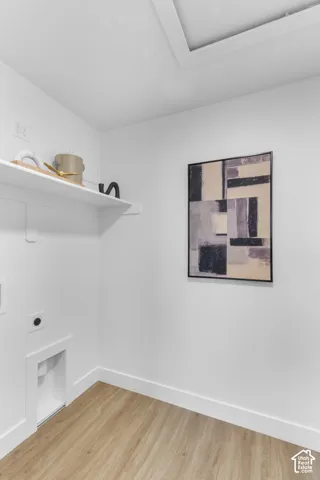 Dedicated laundry area featuring a built-in shelf, light wood-finish flooring, and white baseboards