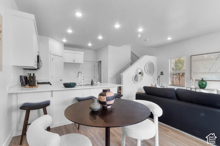 Open-concept living area featuring a kitchen island with seating, recessed lighting, wood-finish flooring, and a staircase with a white railing