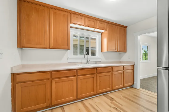 Kitchen featuring light wood cabinetry, light-toned countertops, a stainless steel sink, and wood-finish flooring