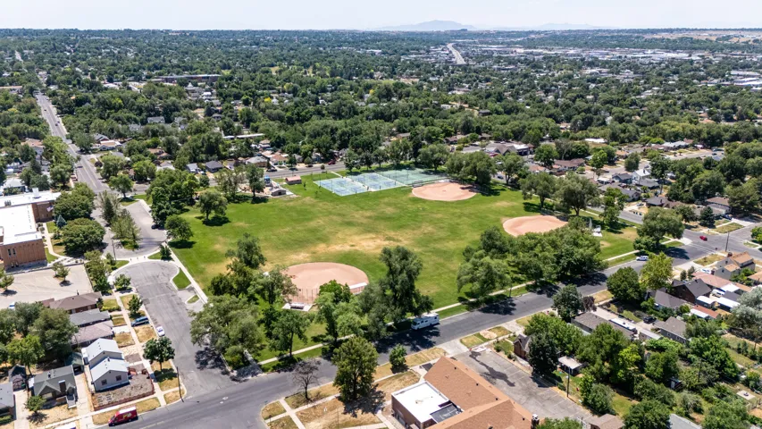 Aerial perspective showcasing a large community park with multiple baseball diamonds and tennis courts, surrounded by tree-lined streets and residential properties