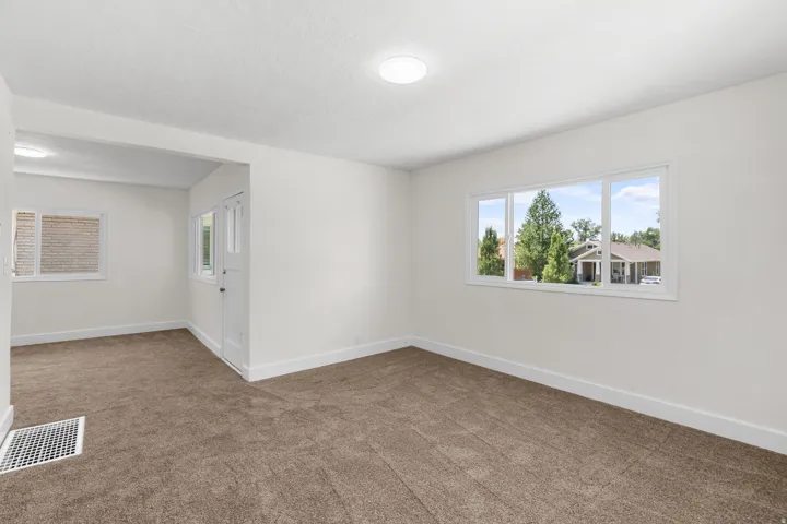 Carpeted interior space featuring an expansive window with a three-pane design, white trim, and a white baseboard