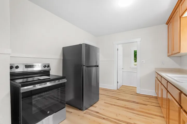 Kitchen featuring stainless steel appliances, wood-finish flooring, light wood cabinetry, and a double basin sink