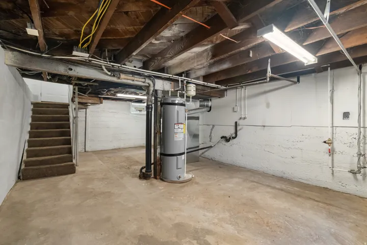 Utility basement space featuring exposed wood joists, concrete flooring, and a water heater