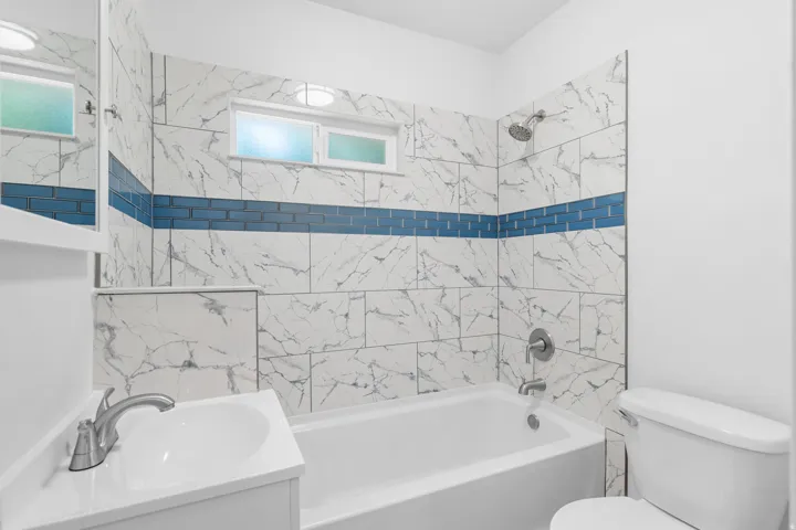 Full bathroom featuring a white bathtub and shower with marble-look wall tiles, accented by a blue subway tile band