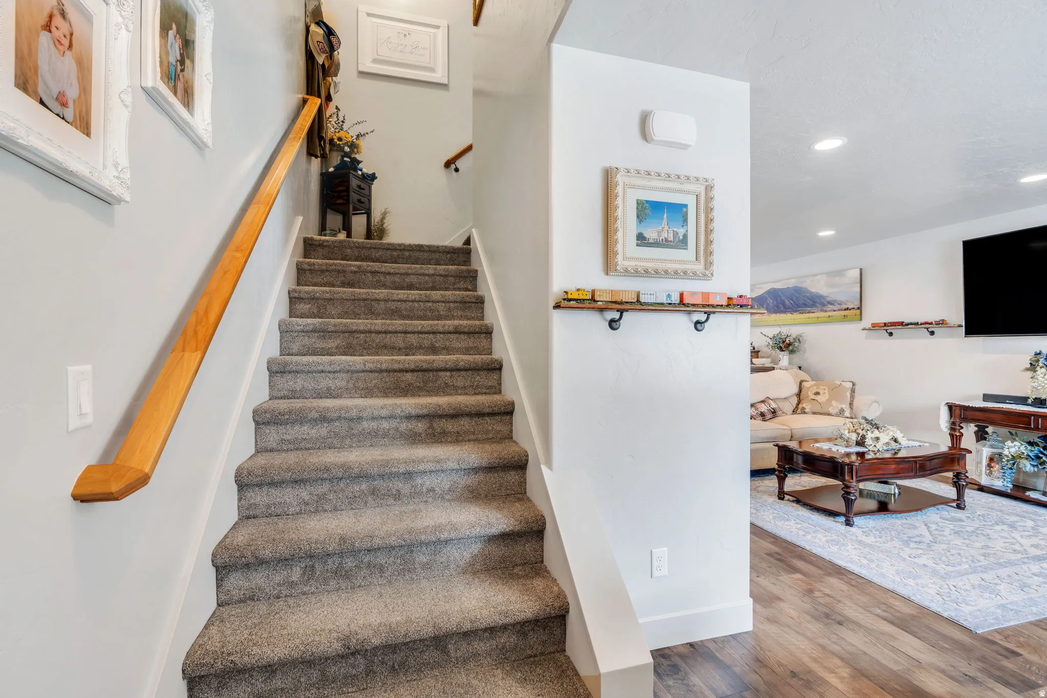 Carpeted staircase with a wood handrail, featuring recessed lighting, white trim, and wood-finish flooring