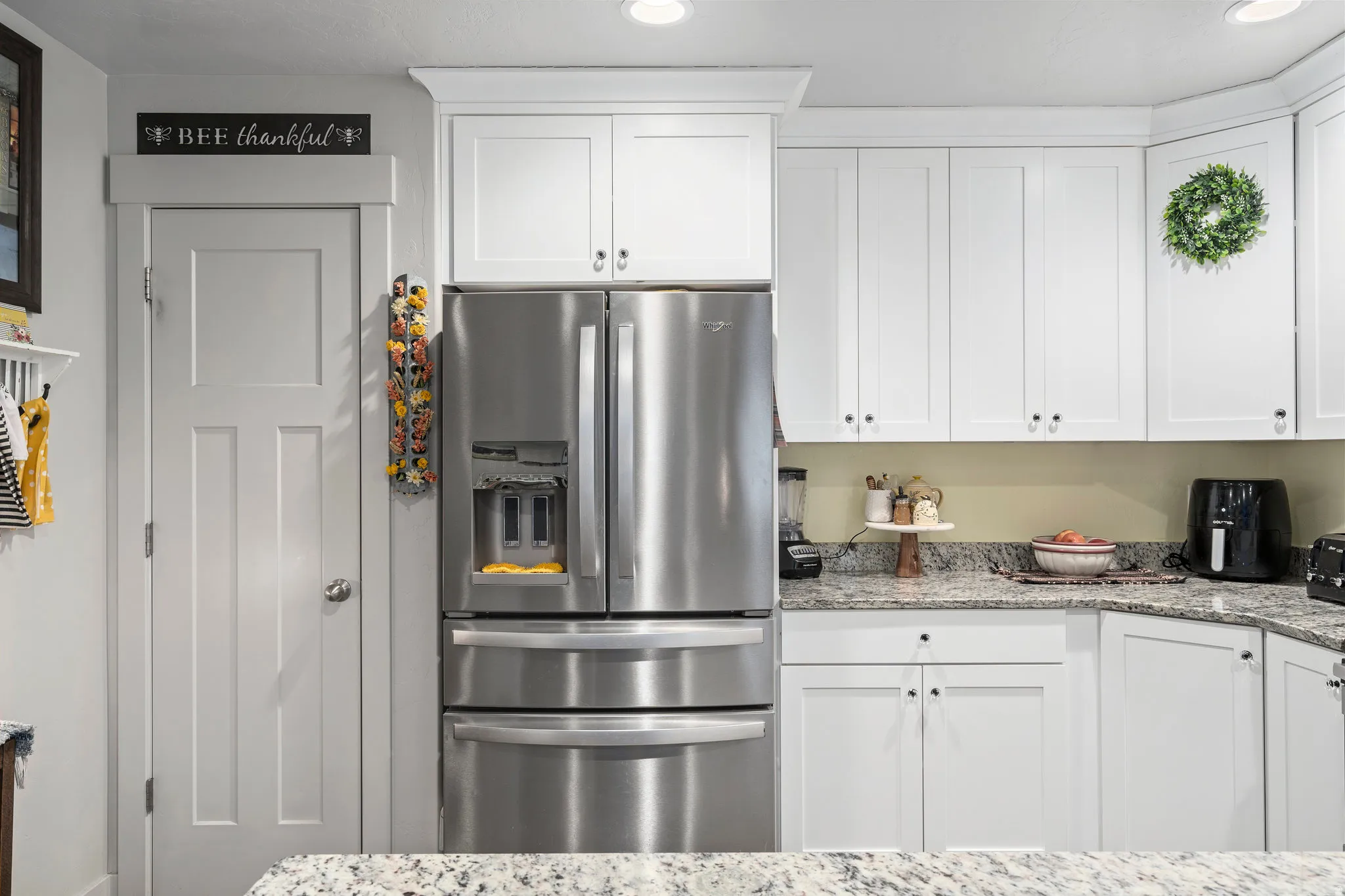 Kitchen featuring white shaker-style cabinetry, stainless steel refrigerator, granite countertops, recessed lighting, and a paneled interior door