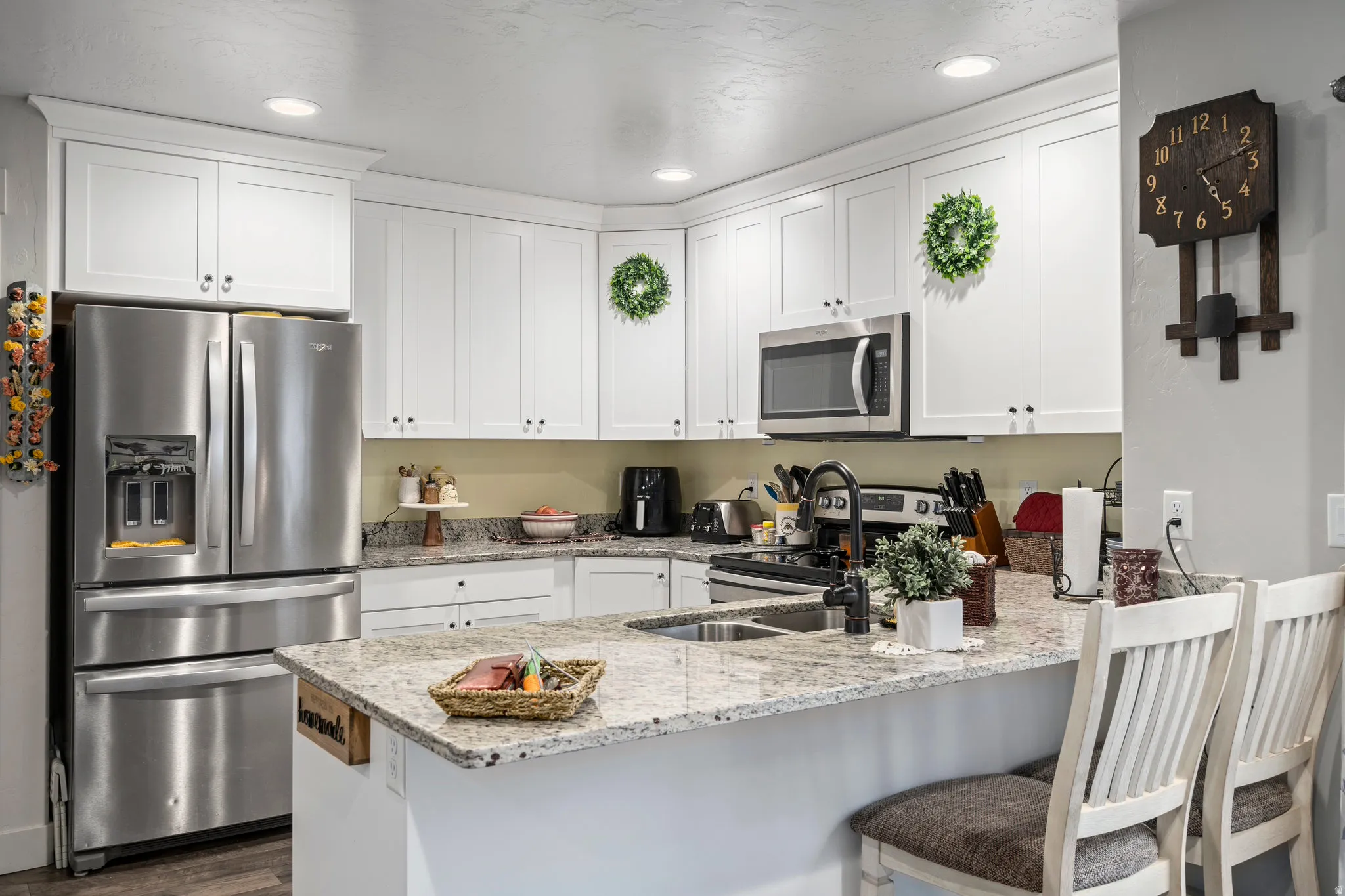 Contemporary kitchen featuring white shaker cabinetry, stainless steel appliances, a multi-tone granite countertop, and recessed lighting
