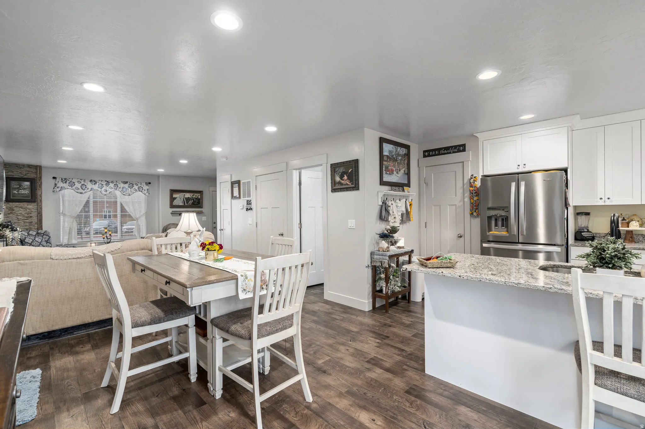 Open-concept living space featuring wood-finish flooring, recessed lighting, white cabinetry, a kitchen island with stone countertops, and a stainless steel refrigerator