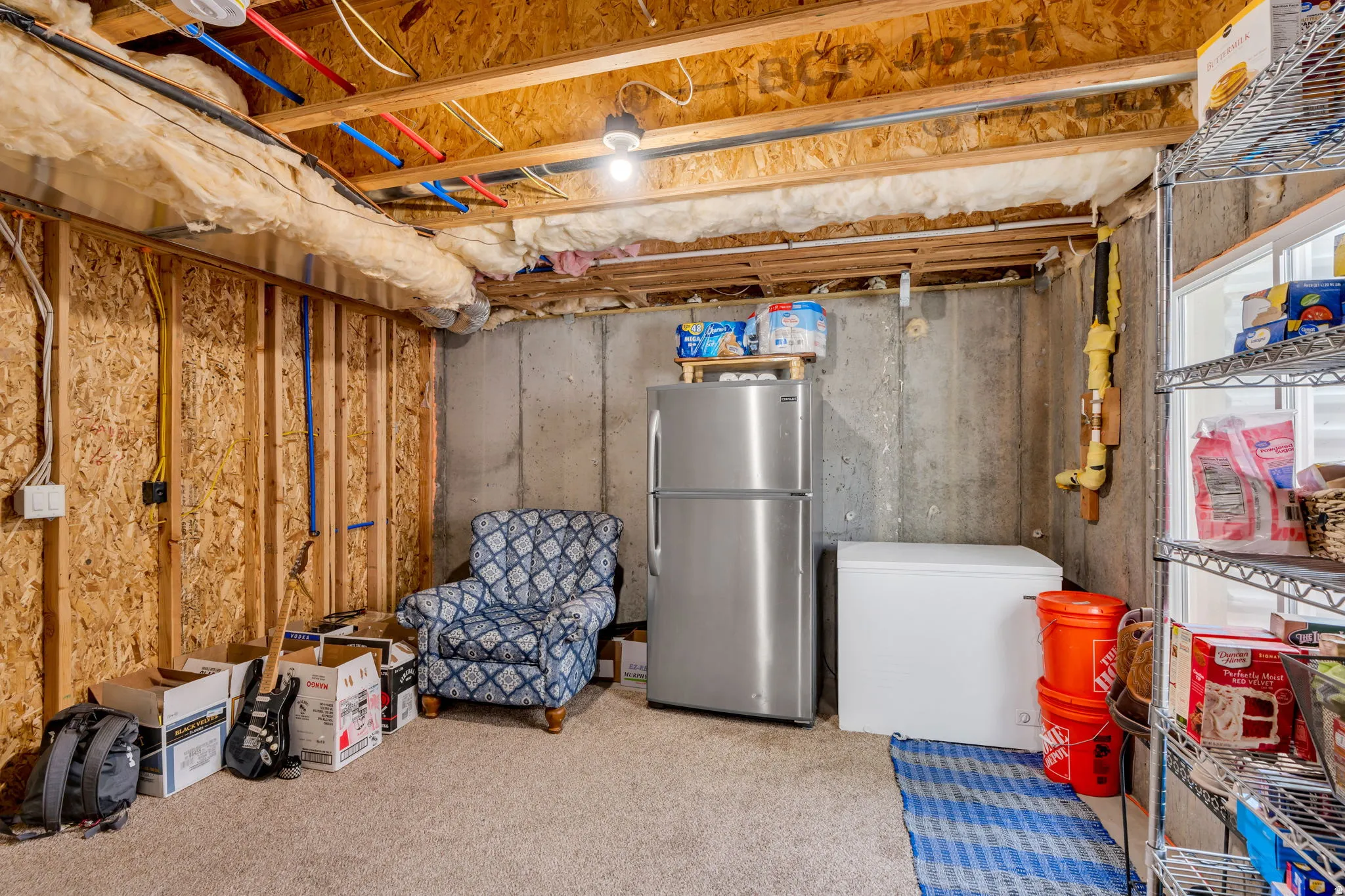 Unfinished basement space featuring exposed wood joists and subflooring, concrete foundation walls, and an insulated ceiling