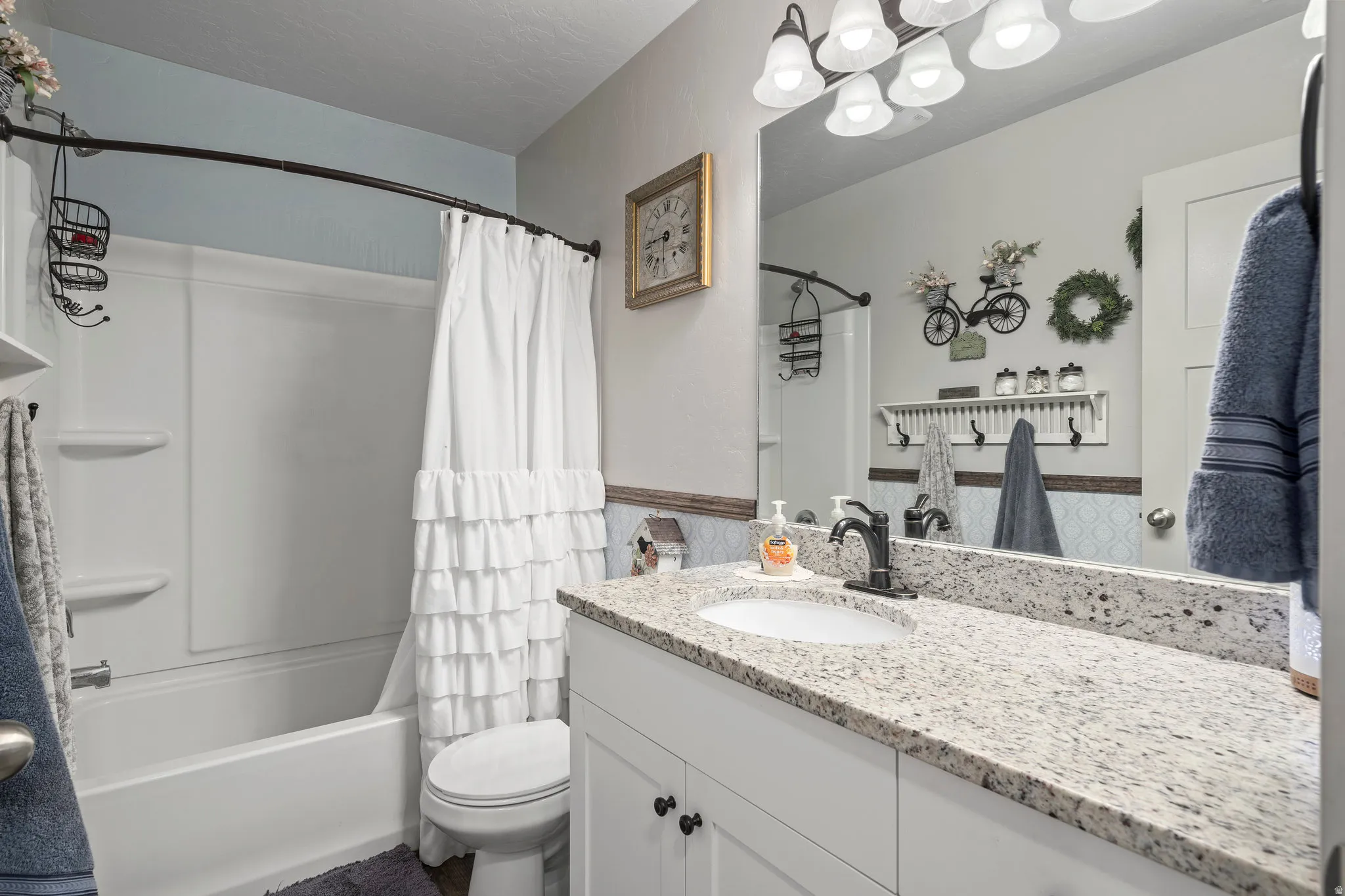 Bathroom featuring a white vanity with a speckled countertop, a large wall-mounted mirror, and a white tub with an integrated shower