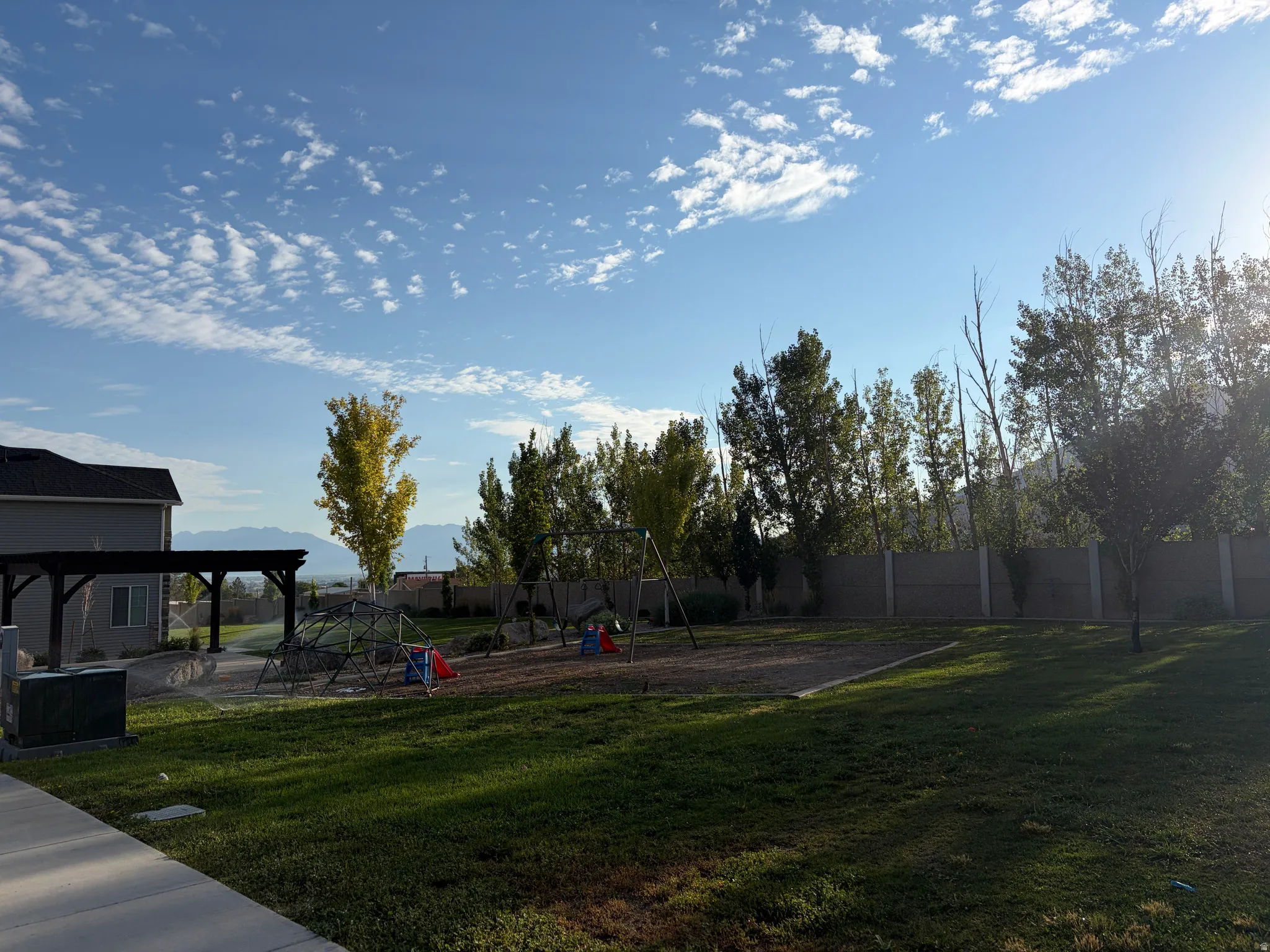 Expansive green space featuring a pergola, swing set, and climbing dome