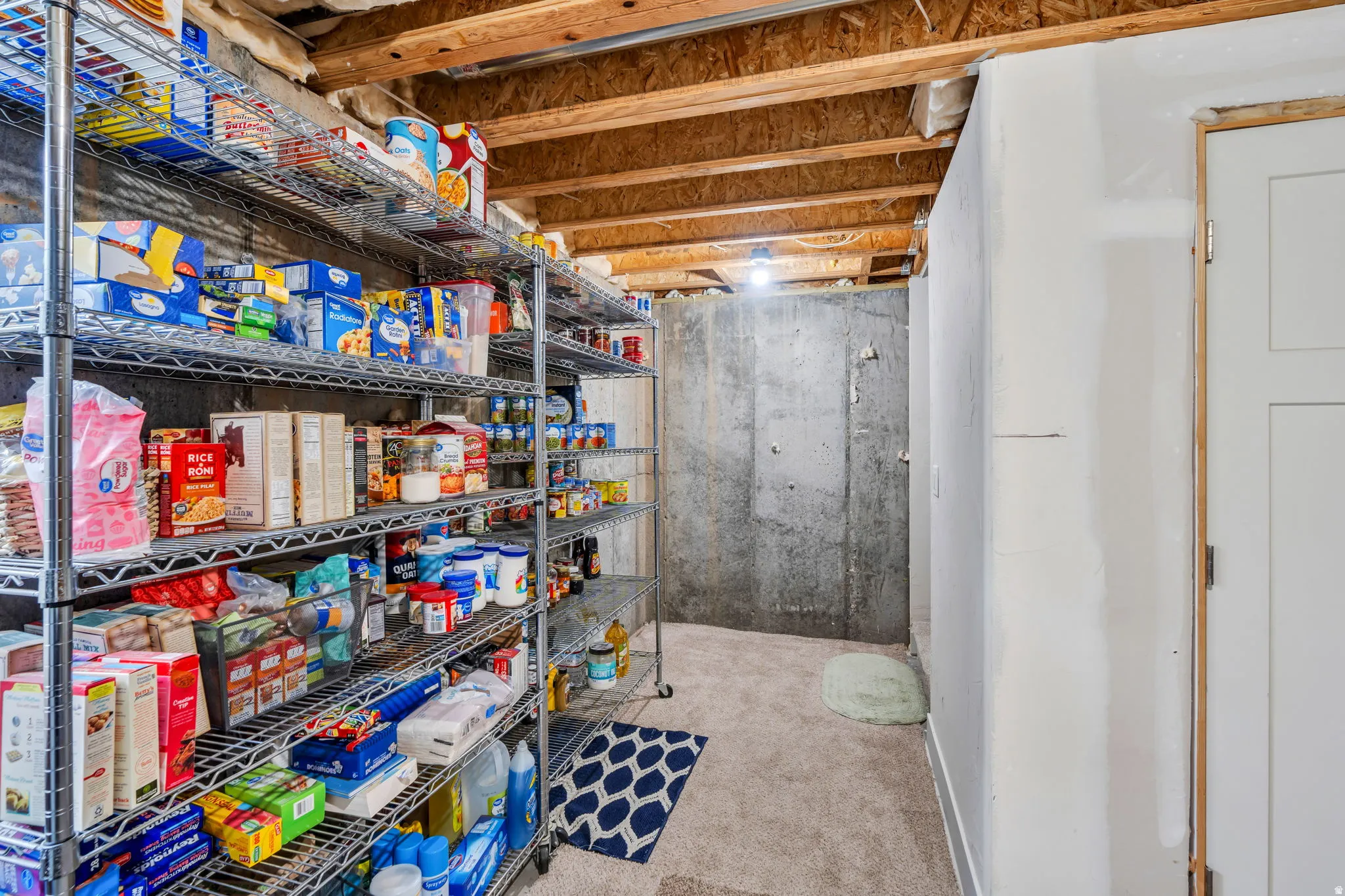Utility room featuring exposed ceiling joists, concrete foundation walls, and a carpeted floor