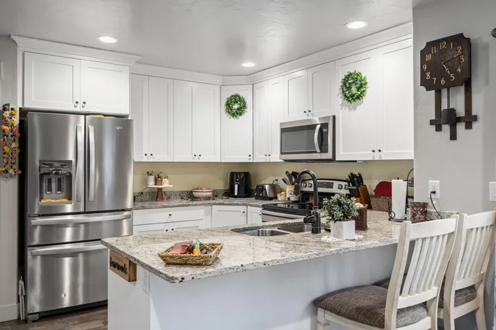 Contemporary kitchen featuring white shaker cabinetry, stainless steel appliances, a multi-tone granite countertop, and recessed lighting