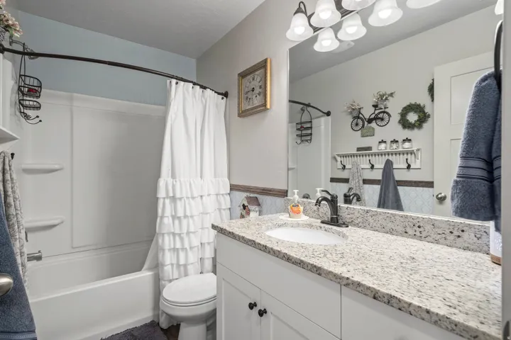 Bathroom featuring a white vanity with a speckled countertop, a large wall-mounted mirror, and a white tub with an integrated shower