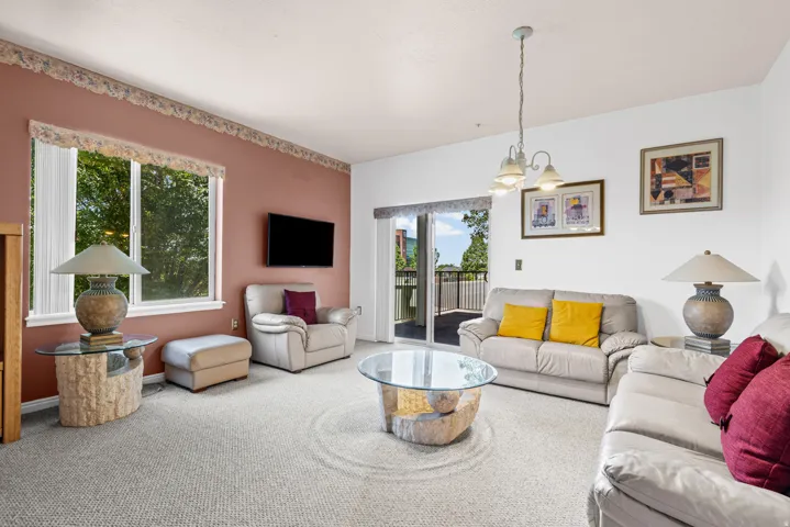 Spacious living area featuring light-toned carpeting, ample natural light from large windows, and a sliding glass door leading to an outdoor balcony