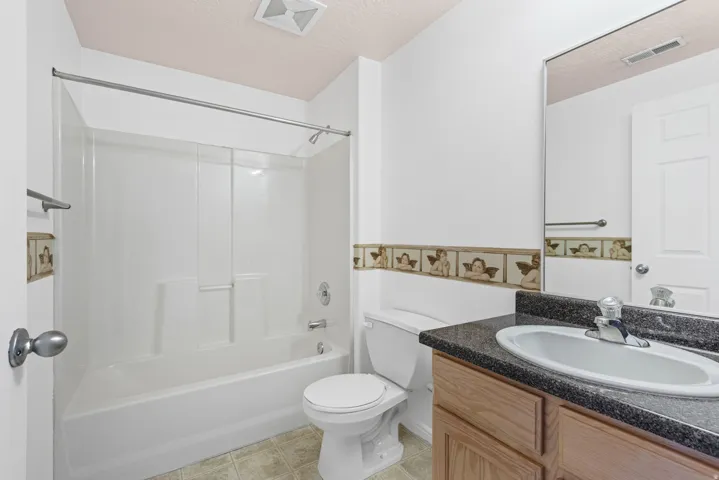 Full bathroom featuring a single vanity with wood-finish cabinetry, a dark speckled countertop, and an integrated sink