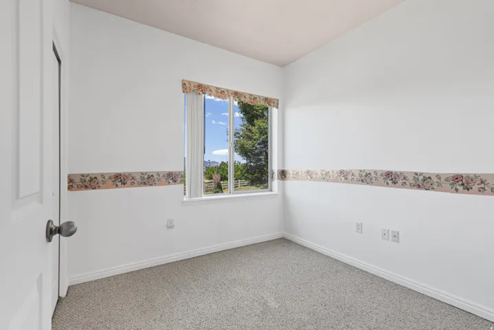 Bright interior space featuring a window with a valance, white walls, and light-toned carpet flooring