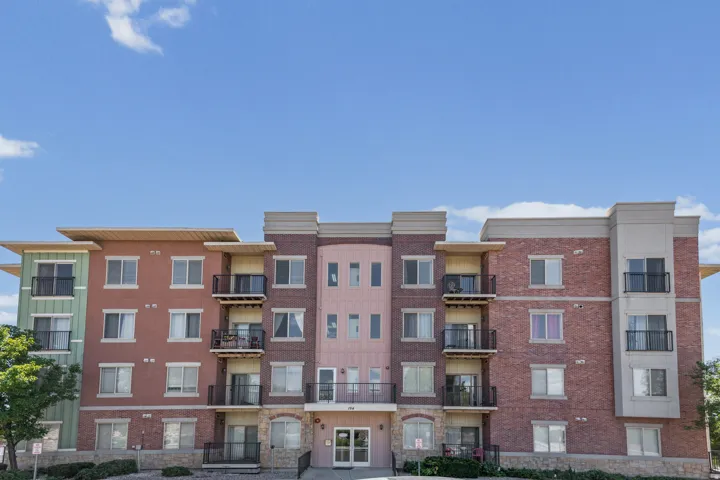 Multi-story apartment building featuring a brick and stucco exterior, individual balconies with black railings, ground-level entryways, and stone accents
