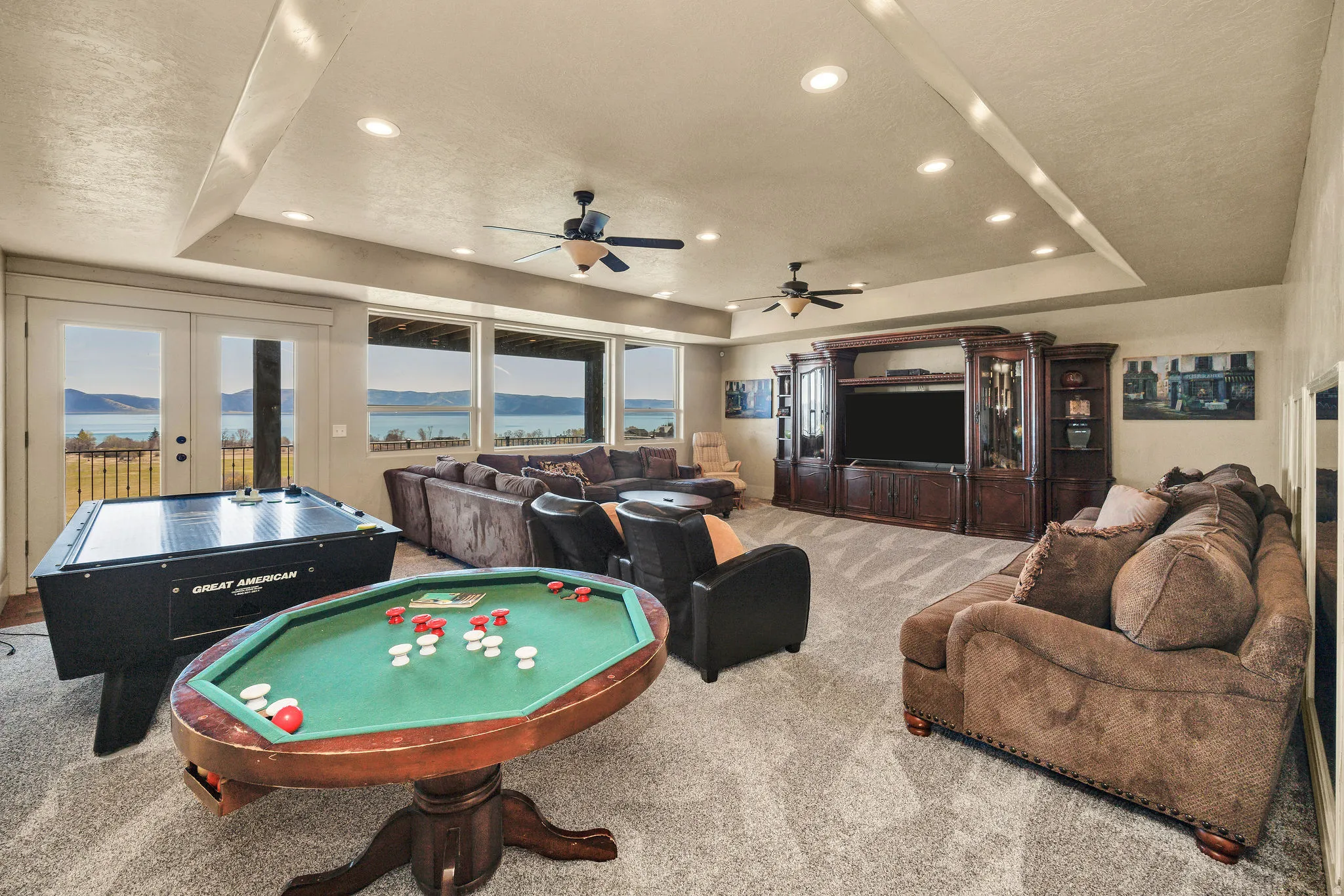 Expansive entertainment area featuring large windows, a tray ceiling with recessed lighting, French doors, and carpeting