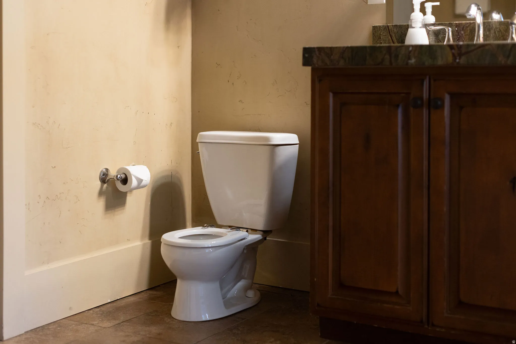 Bathroom featuring a white toilet, dark wood vanity with a stone countertop, and textured beige walls