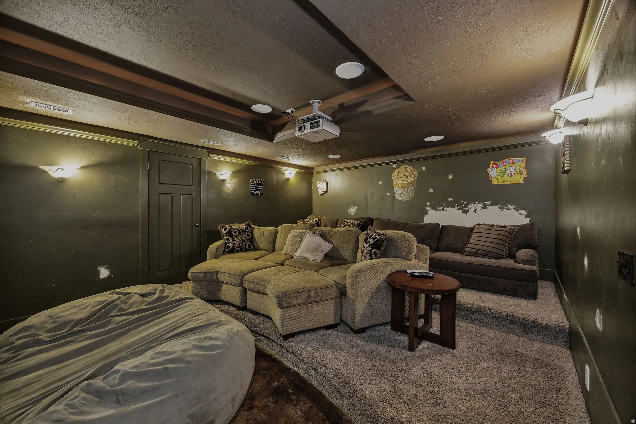 Dedicated media room featuring tiered seating, recessed ceiling lighting, wall sconces, and a ceiling-mounted projector