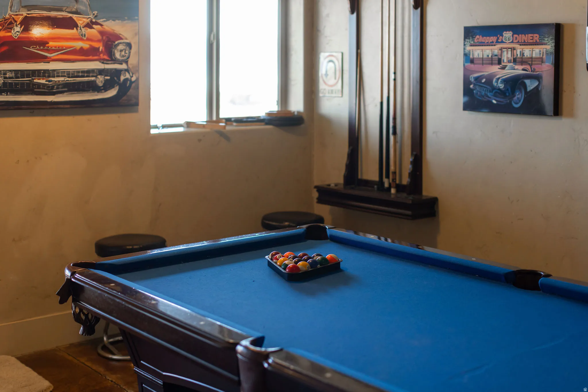 Recreation area featuring a pool table with blue felt, a cue rack with cues, and a window with natural light