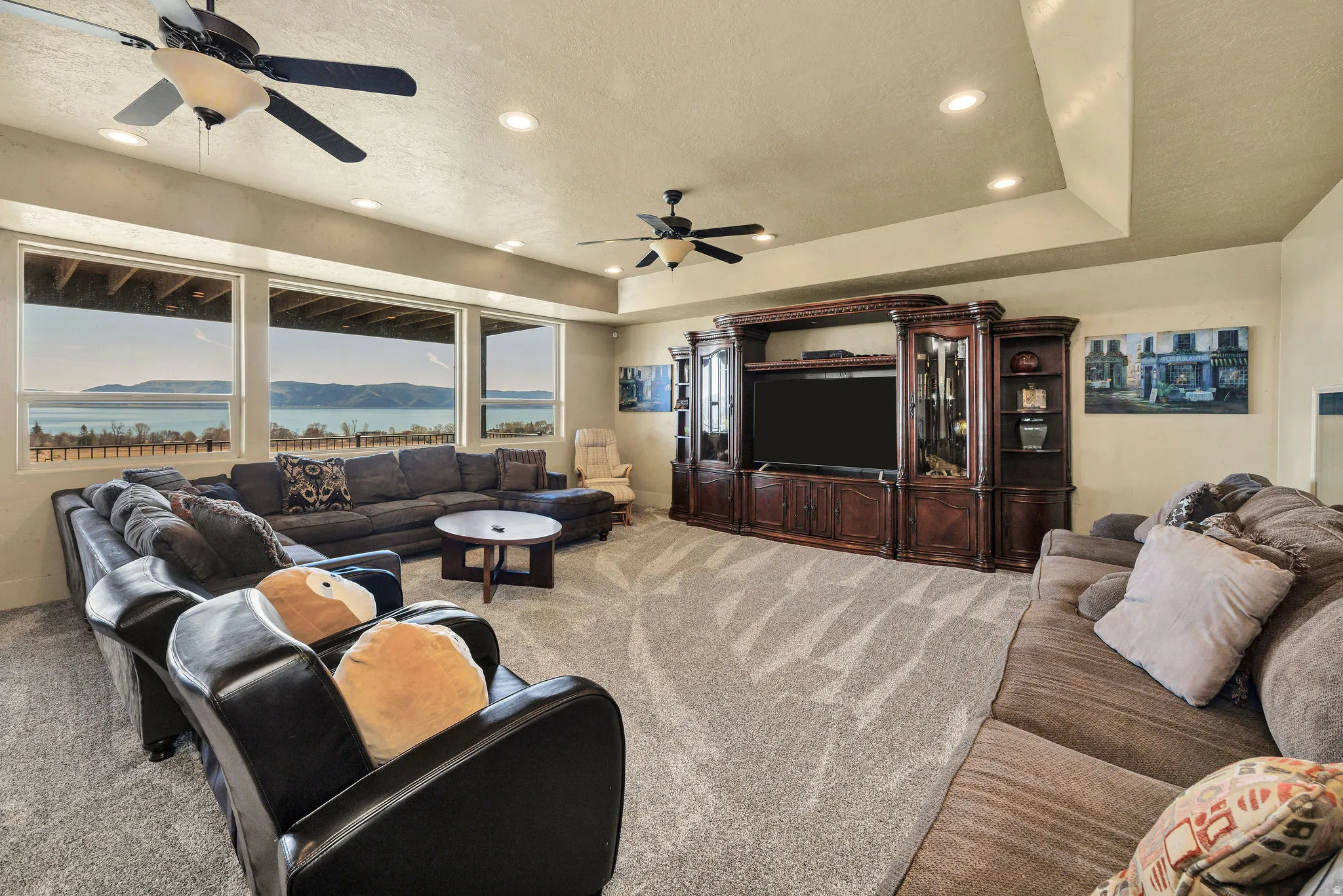 Spacious entertainment area featuring a wide carpeted floor, built-in media console, multiple recessed lights, and tray ceiling detail