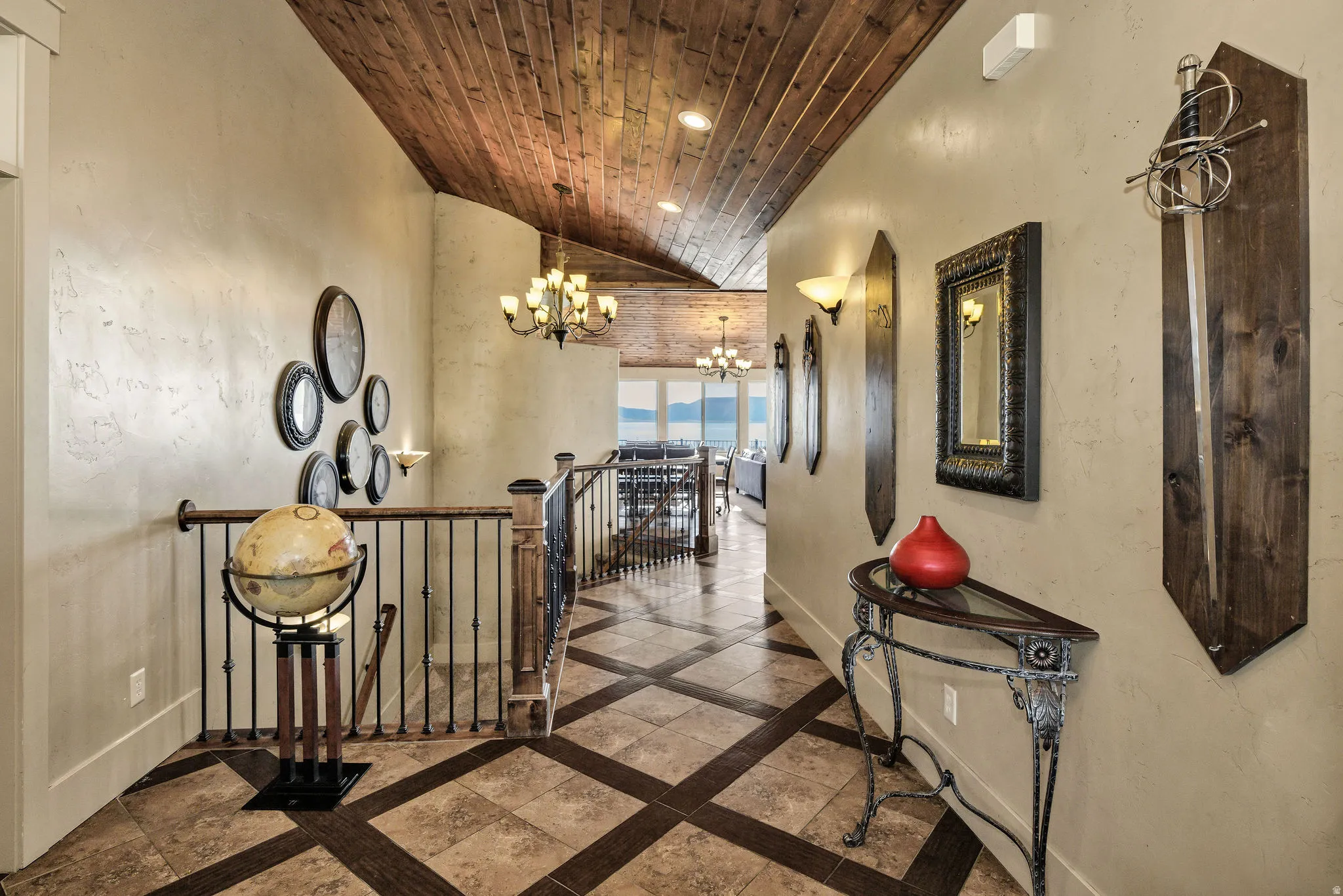 Hallway featuring wood-finish ceiling, patterned tile flooring, wrought iron railings, and sconce lighting