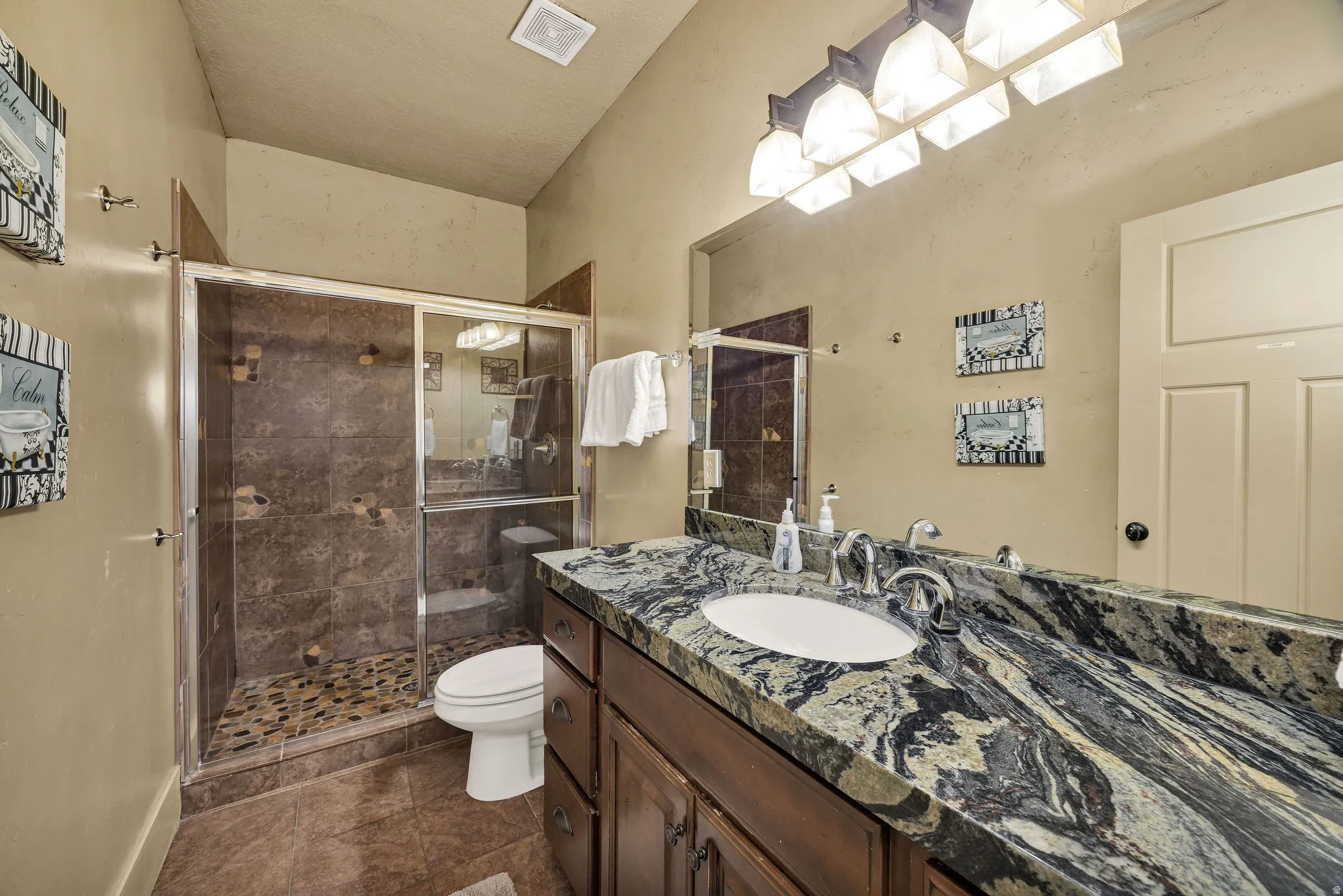 Bathroom featuring a spacious vanity with an elongated undermount sink, a richly patterned countertop, and a dark wood-finish cabinet