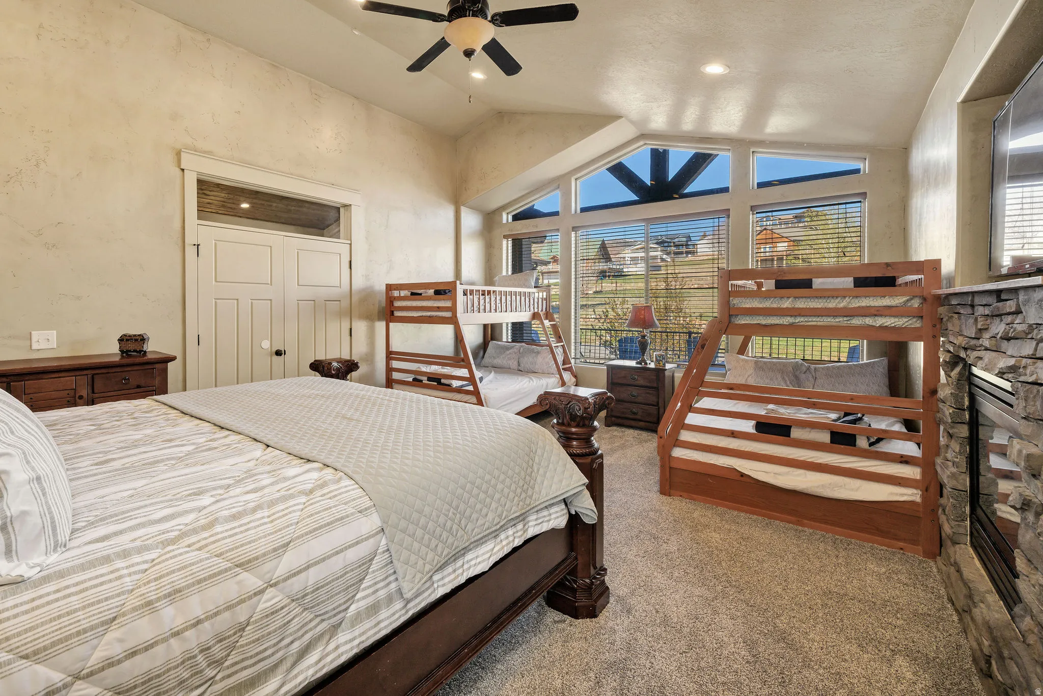 Bedroom featuring vaulted ceilings, a stone-faced fireplace, and expansive windows