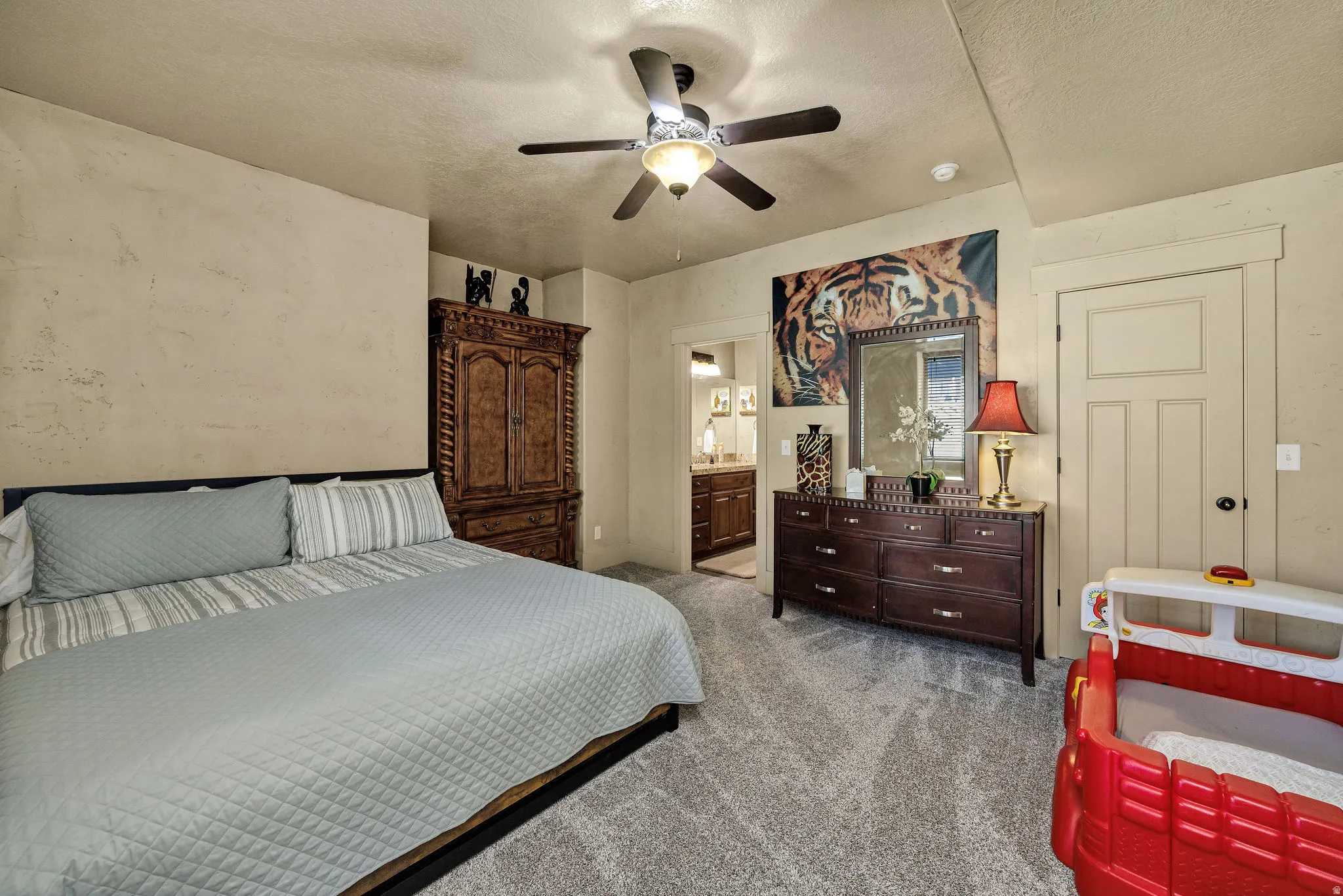 Bedroom featuring light-toned walls, textured carpet flooring, and a ceiling fan with integrated lighting