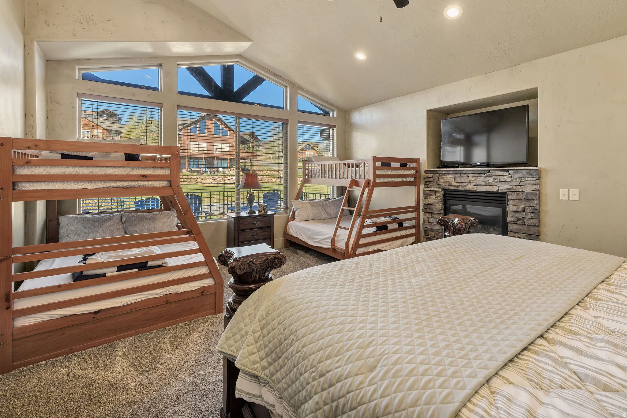 Spacious room featuring vaulted ceilings, a stone-faced fireplace with a built-in media niche, and large windows with integrated blinds