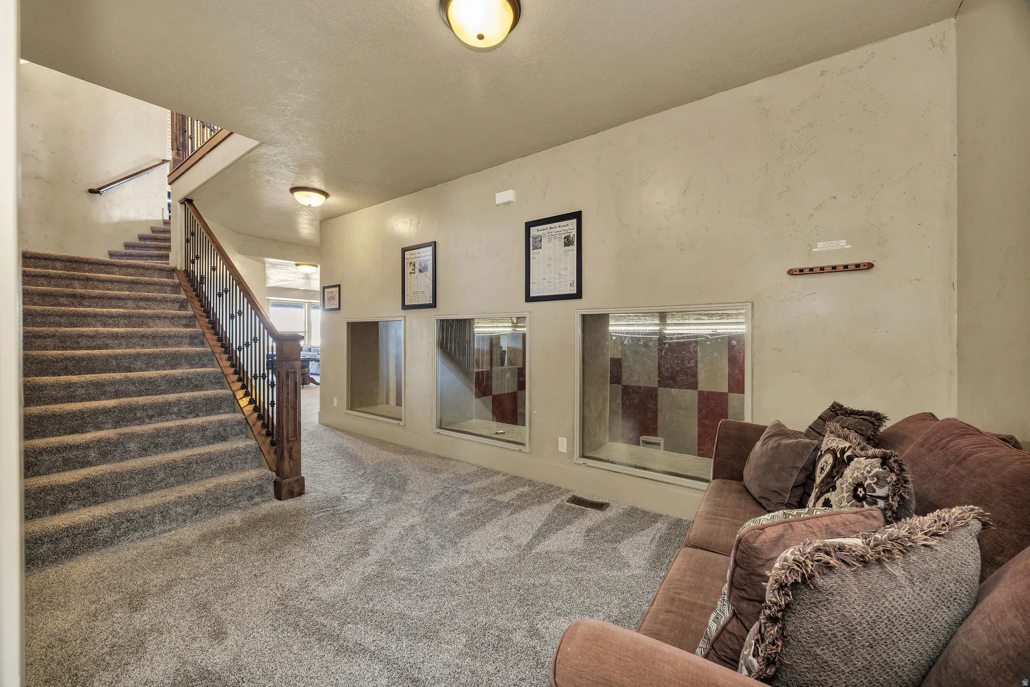 Carpeted staircase with dark wood newel post and wrought iron balusters